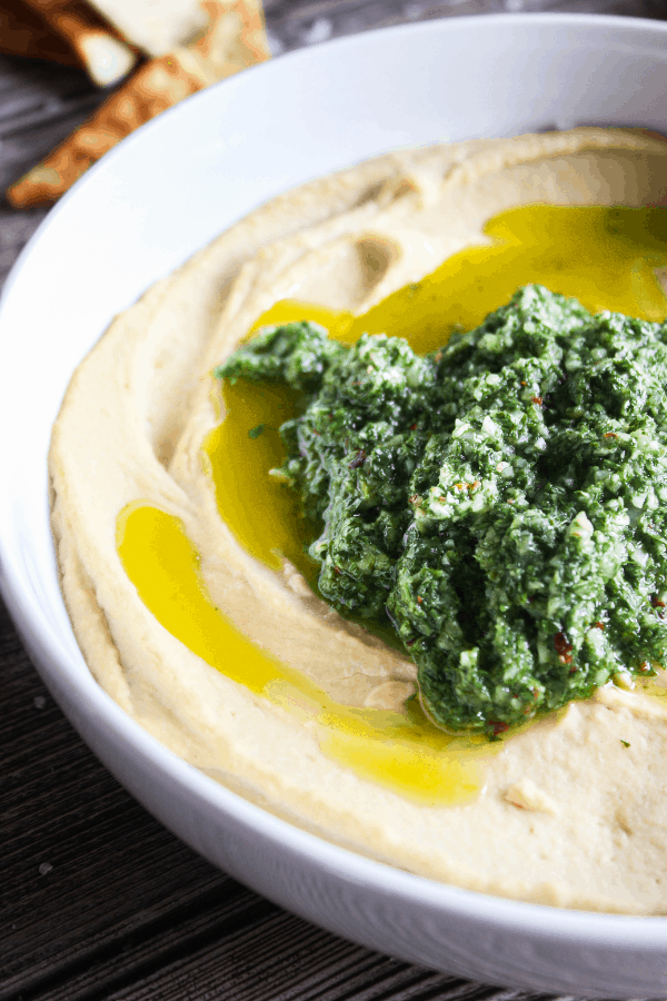 Half bowl of chimichurri hummus with pita chips in background.