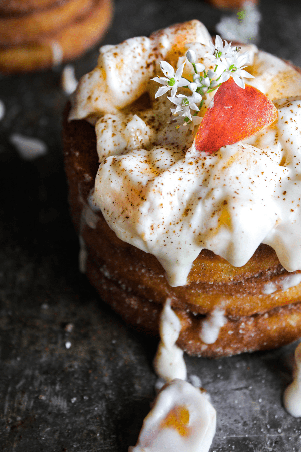 Close-up shot of stack of churro waffles with peaches and cream garnished with small white flowers.