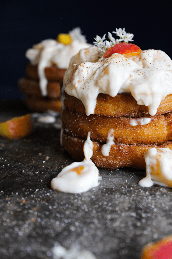A stack of churro waffles with peaches and cream and a second stack in the background.