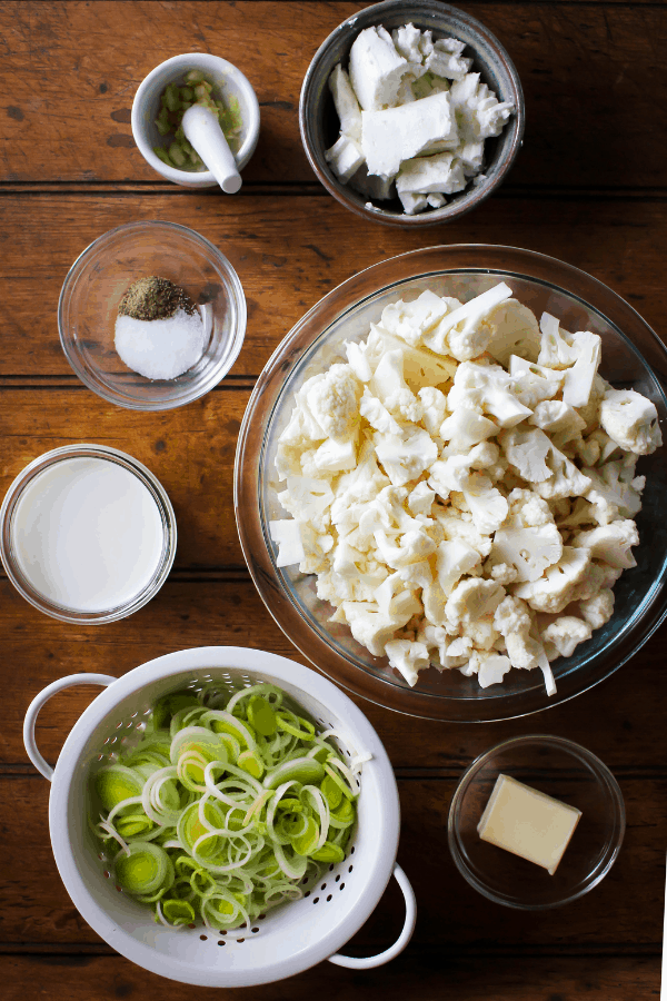 Top down shot of ingredients for goat cheese mashed cauliflower with sautéed leeks on a wood surface.