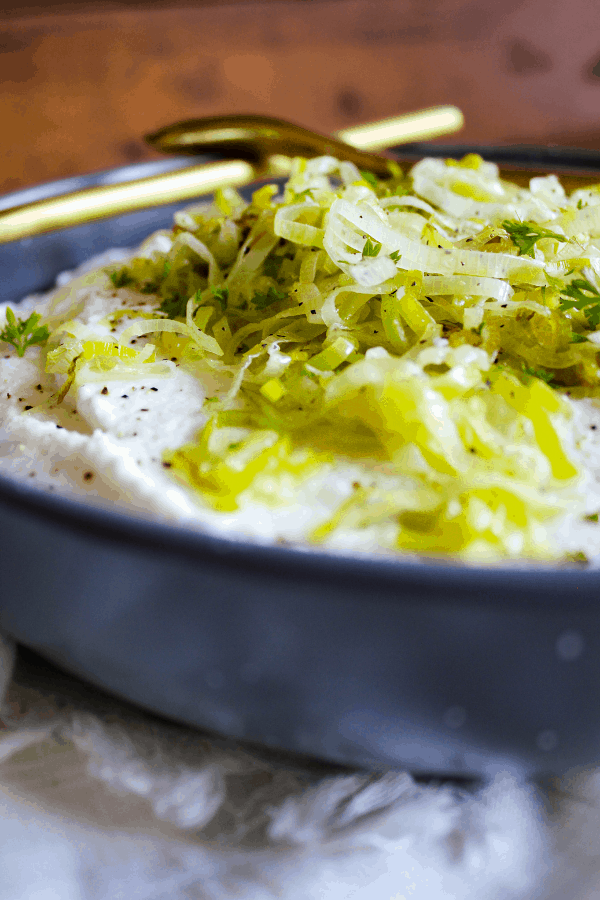 Bowl of mashed cauliflower with sautéed leeks with a spoon set across the top.
