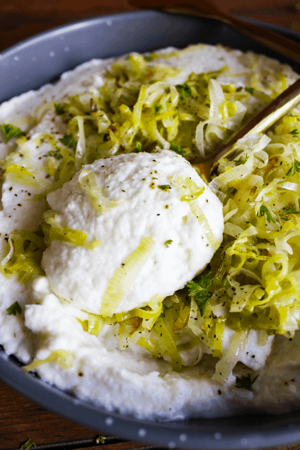 Close-up shot of spoonful of mashed cauliflower with bowl full in background.