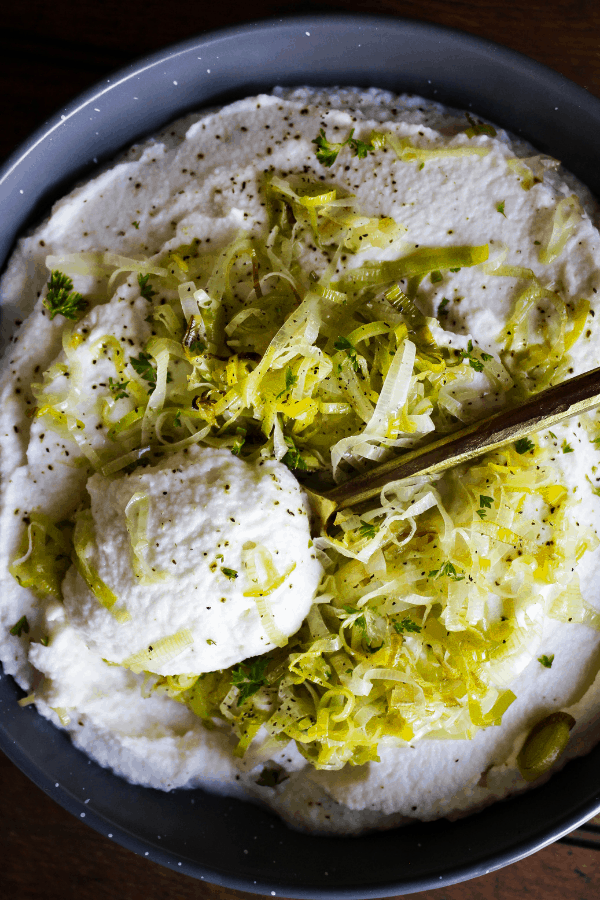 Top down shot of mashed cauliflower topped with sautéed leeks and a spoon of cauliflower mash sitting top it.