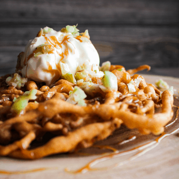 Caramel apple funnel cake topped with vanilla ice cream on a tree trunk platter.