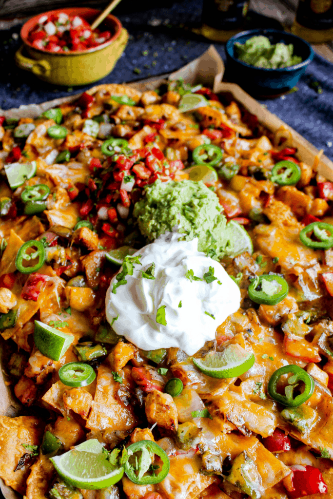Sheet pan loaded with chicken fajita nachos topped with sour cream, guacamole, and pico.