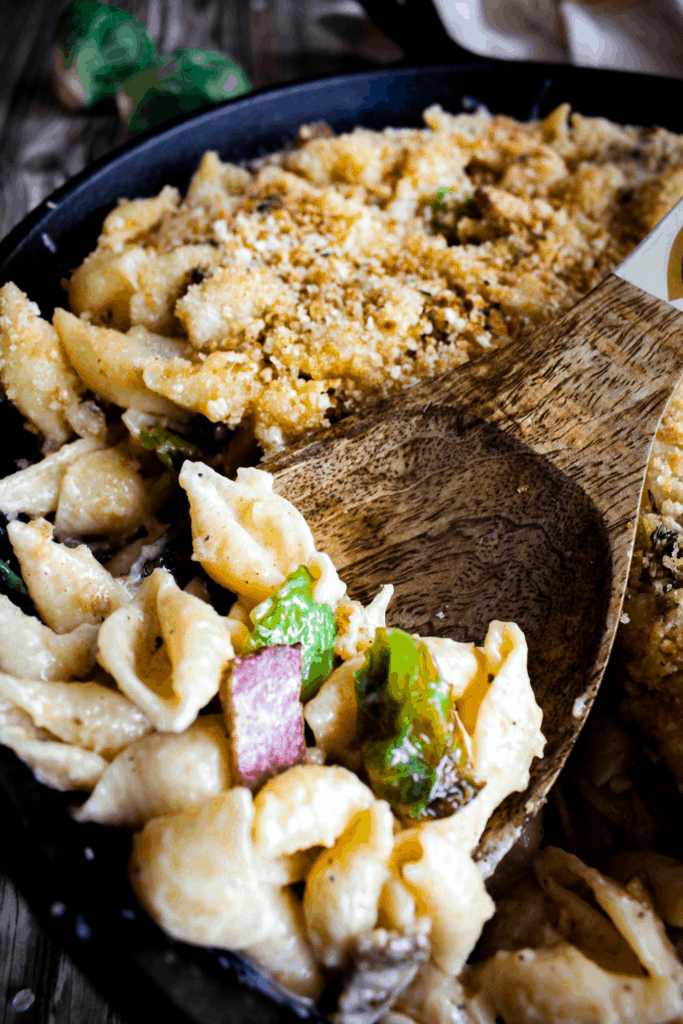 Close-up of wooden spoonful of mac and cheese with Brussels sprouts and bacon atop a pan of mac and cheese.