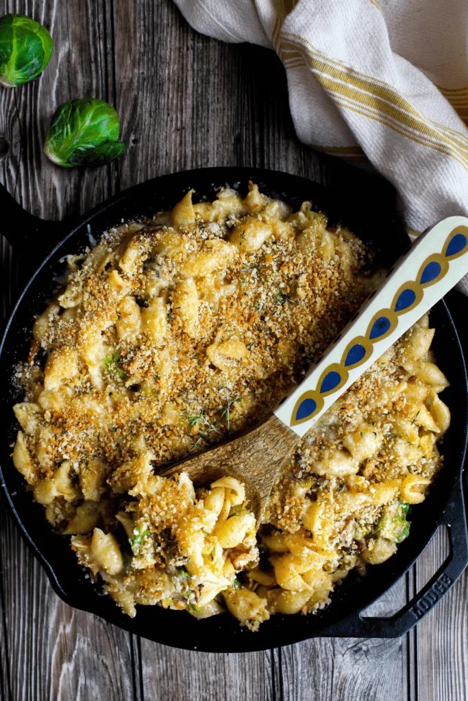 Tablescape with pan of mac and cheese with scattered salt, Brussels sprouts, and yellow dish towel.