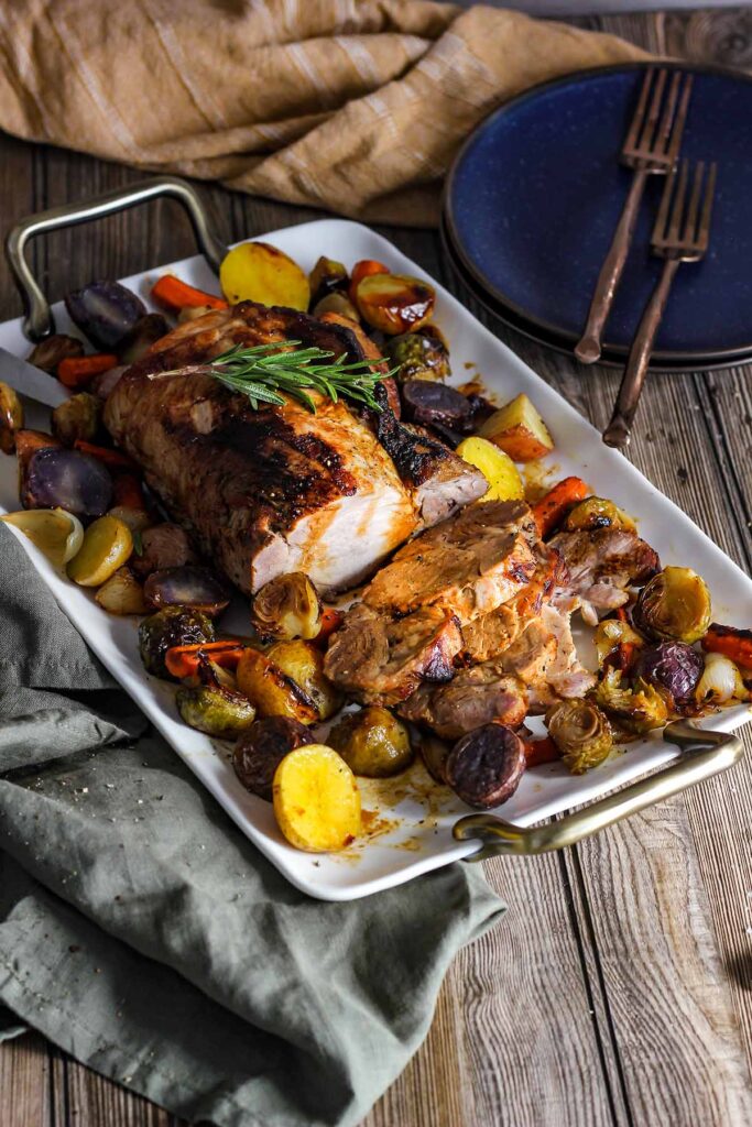 Pork roast garnished with rosemary and surrounded by veggies on a platter.