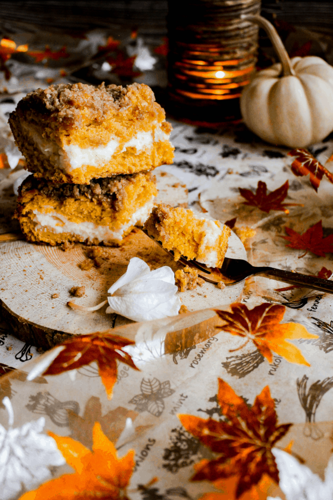 Two slices of pumpkin coffee cake on wood platter with a fork and fall decorations.