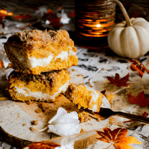 Two slices of pumpkin coffee cake on wood platter with a fork and fall decorations.