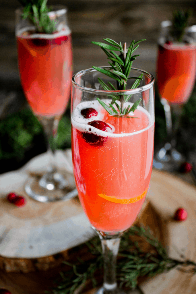 Three champagne flutes full of cranberry orange mimosa on a table scape with greenery and scattered cranberries.