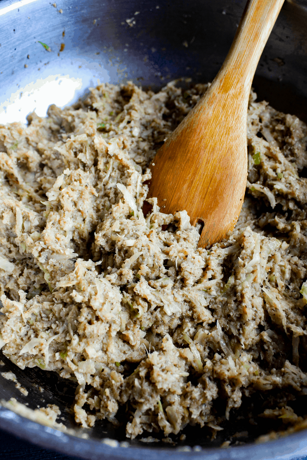 Dumpling filling in sauté pan with a wooden spoon.