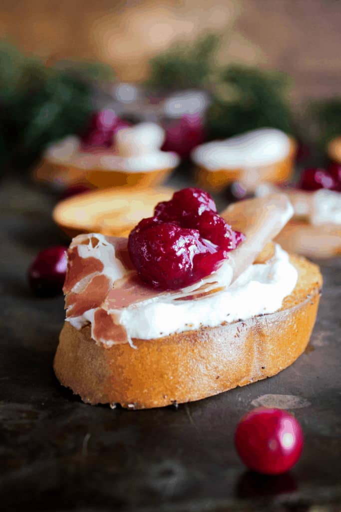 Whipped goat cheese crostini with prosciutto and cranberry sauce with additional crostini in background.