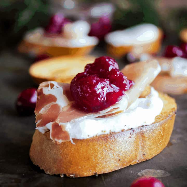 Whipped goat cheese crostini with prosciutto and cranberry sauce with additional crostini in background.
