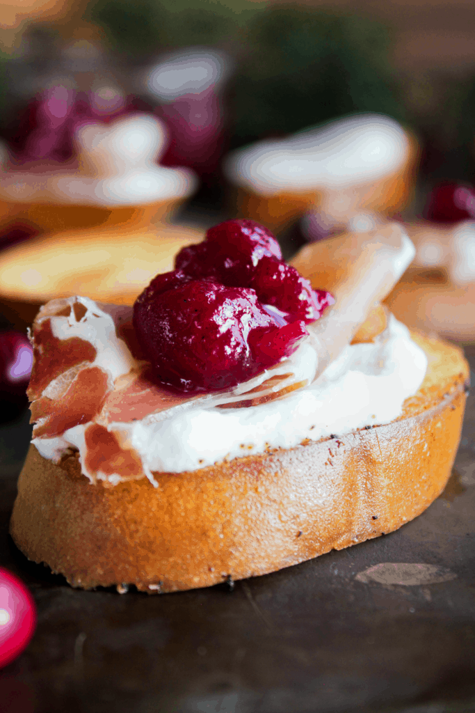 Close up of crostini with goat cheese, proscuitto, and cranberry sauce.