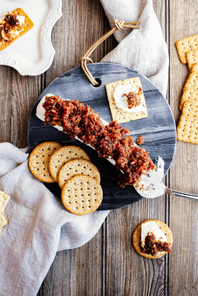 Top down shot of tablescape with platter of goat cheese log with bacon date jam and multiple stacks of crackers.