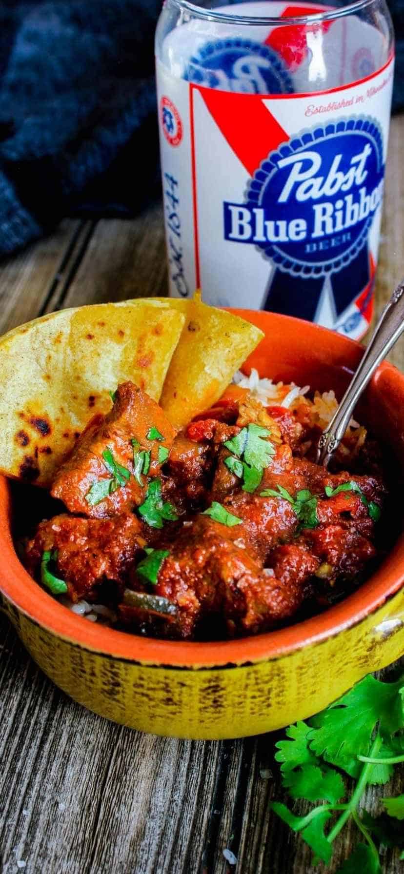 A bowl of spicy pork chili with quesadillas and a PBR glass.