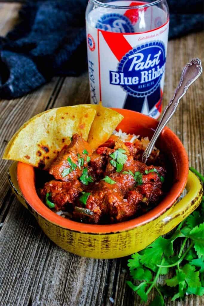 A bowl of spicy pork chili with quesadillas and a PBR glass.