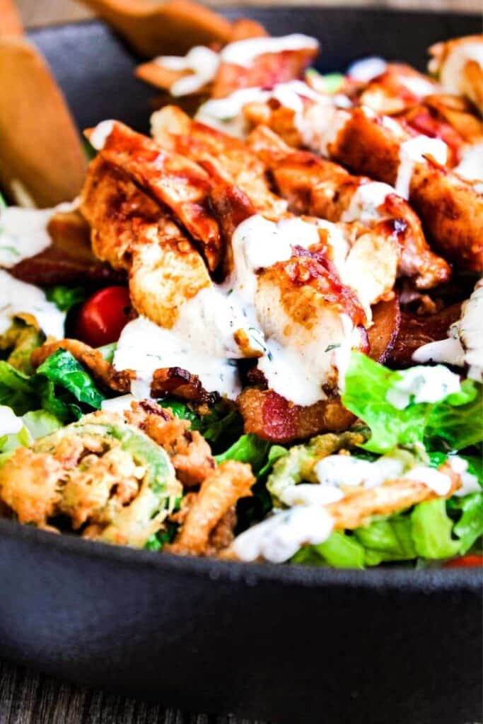Close up of bbq chicken bacon ranch salad with tongs.