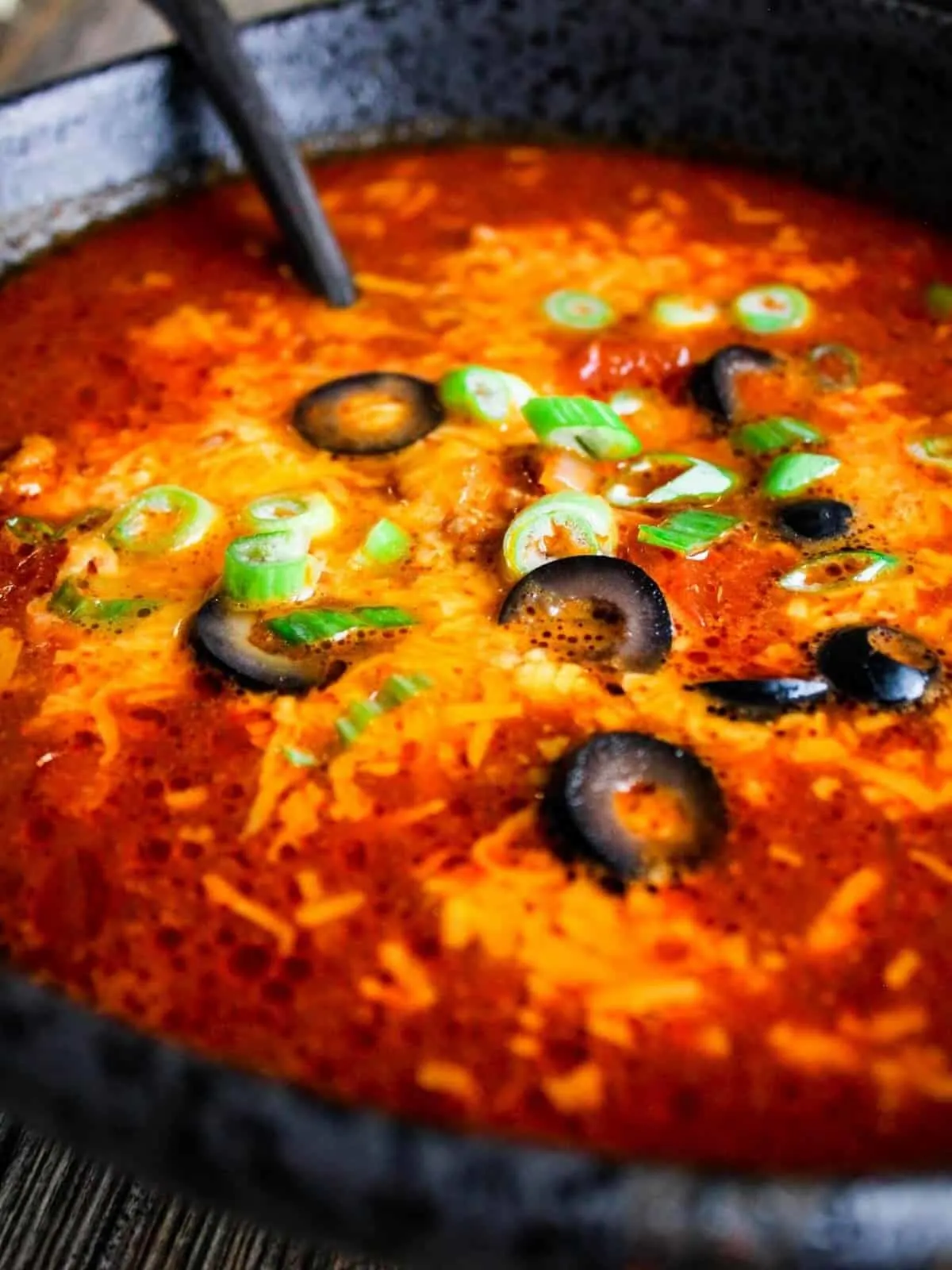 Close-up of beef enchilada soup topped with black olives and green onions.