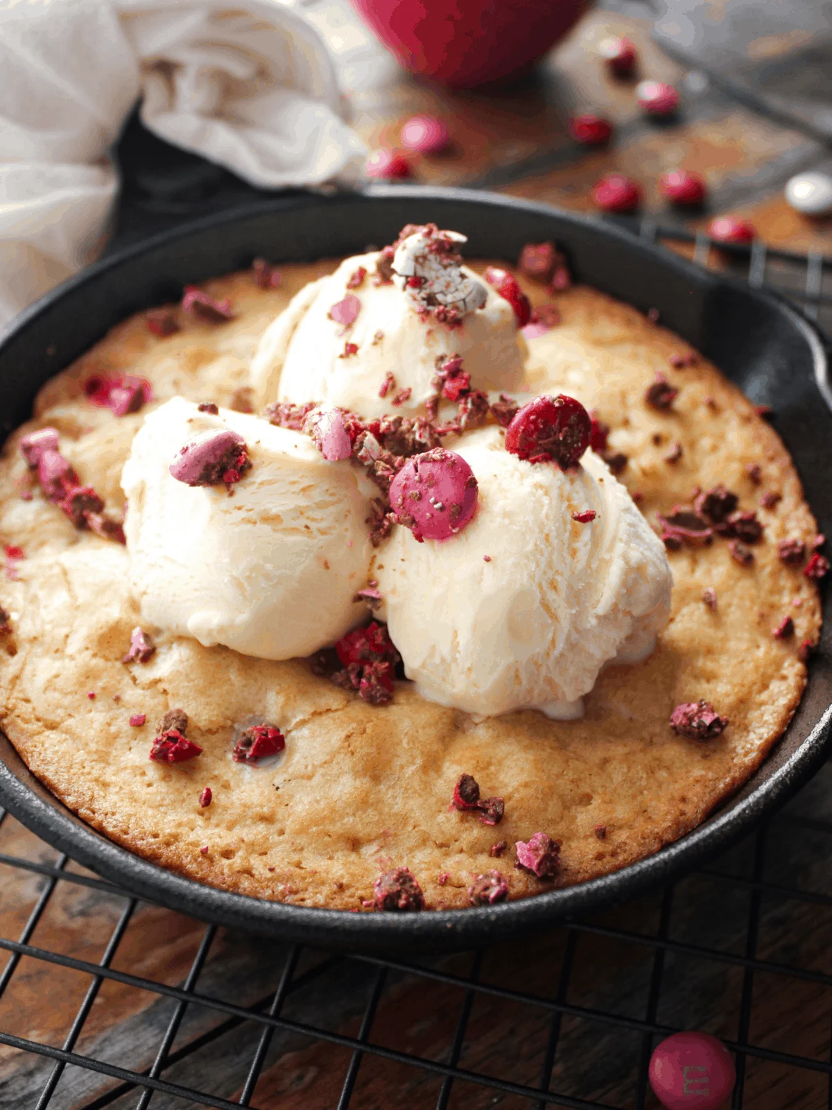 Blondie in a cast iron skillet with three scoops of ice cream and crushed red and pink M&M's.