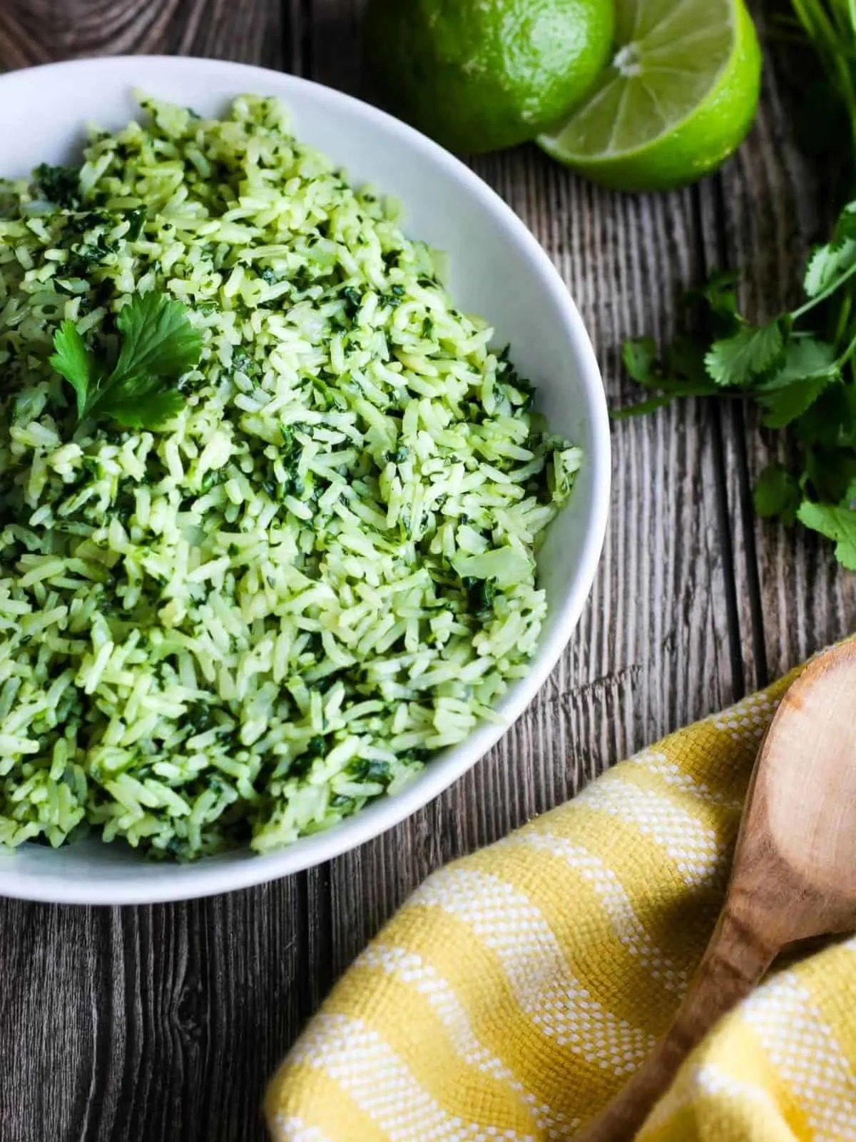Bowl of rice with a yellow towel, wooden spoon, and limes.