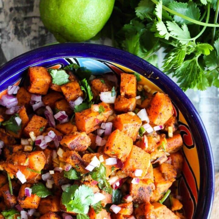 Colorful bowl of sweet potato salad with a lime and a bunch of cilantro.