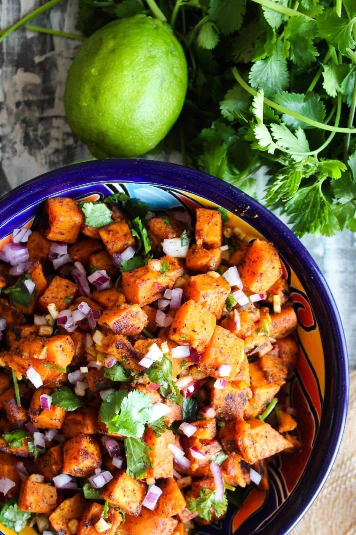 Colorful bowl of sweet potato salad with a lime and a bunch of cilantro.