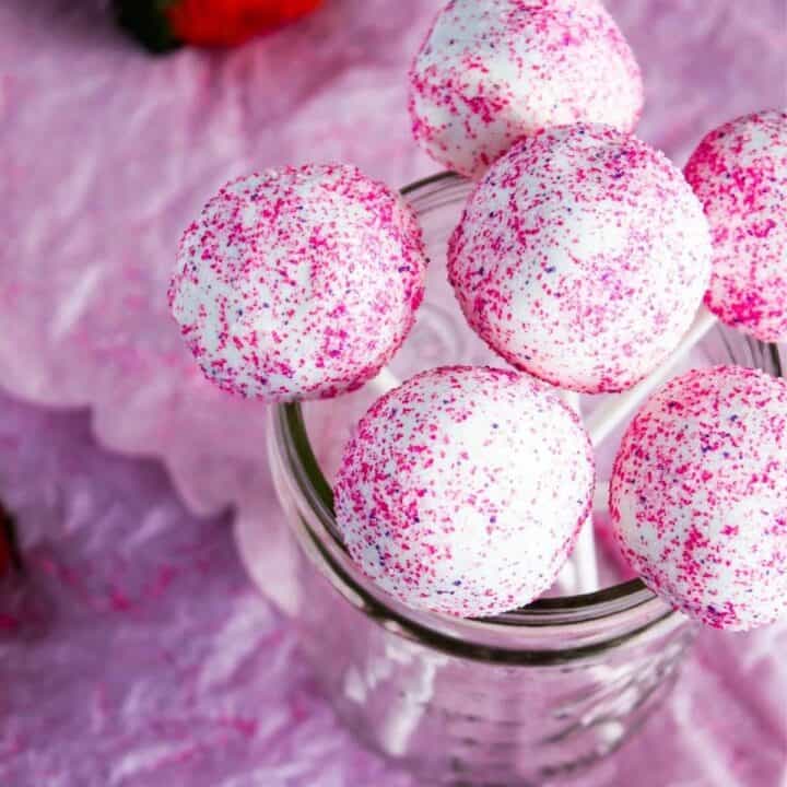 Glass jar filled with cake pops with scattered strawberries.