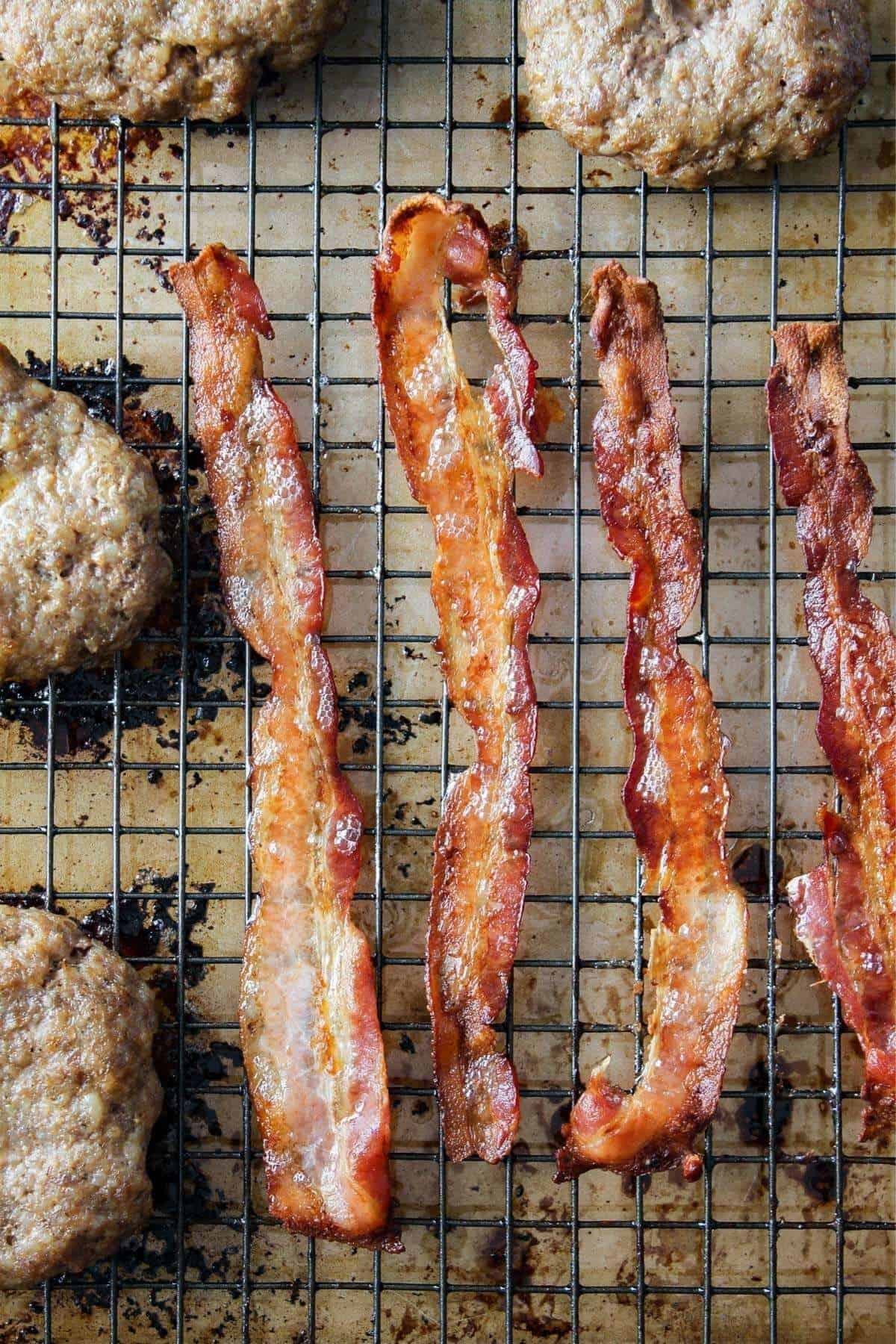 Sausage patties and bacon on a wire cooling rack.