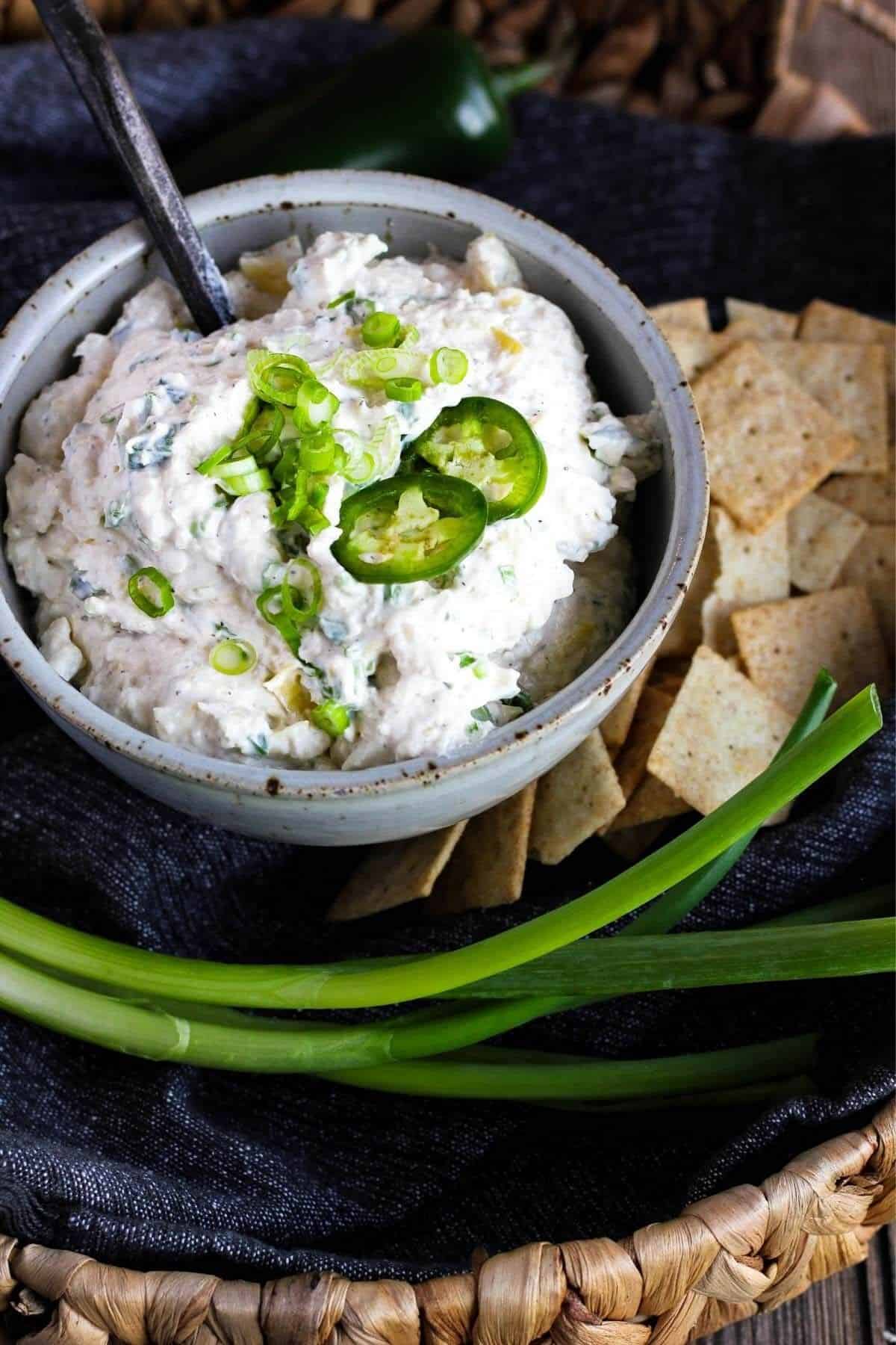 Bowl of jalapeno artichoke dip with crackers and green onion stalks.