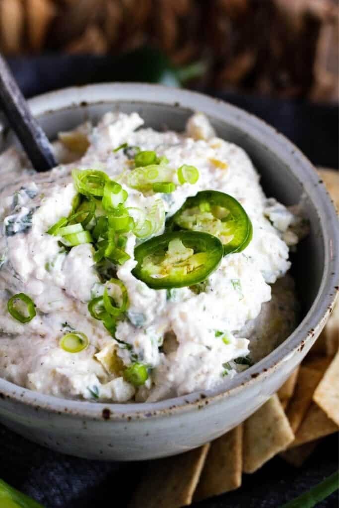 Bowl of creamy artichoke dip with jalapenos and a spoon.