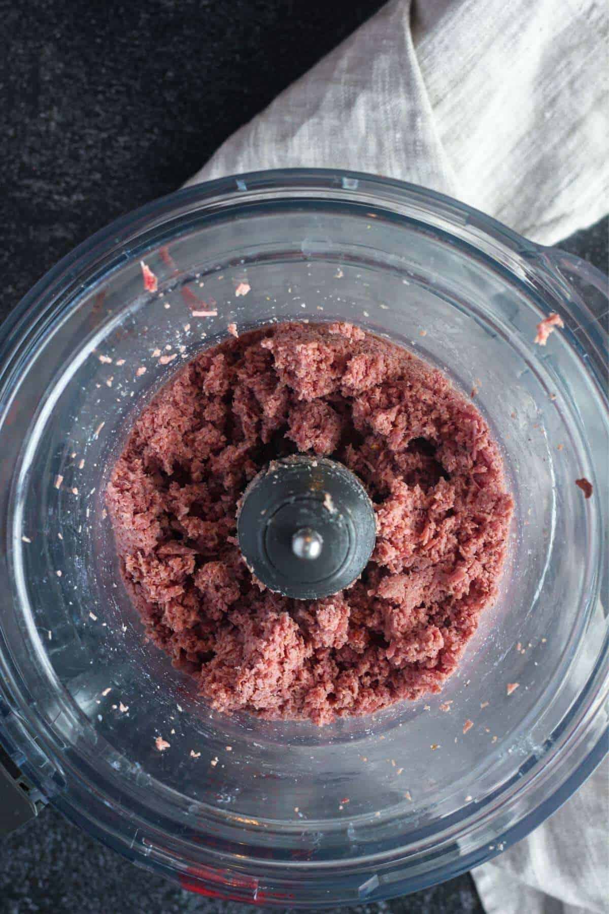 Ground corned beef in food processor bowl.