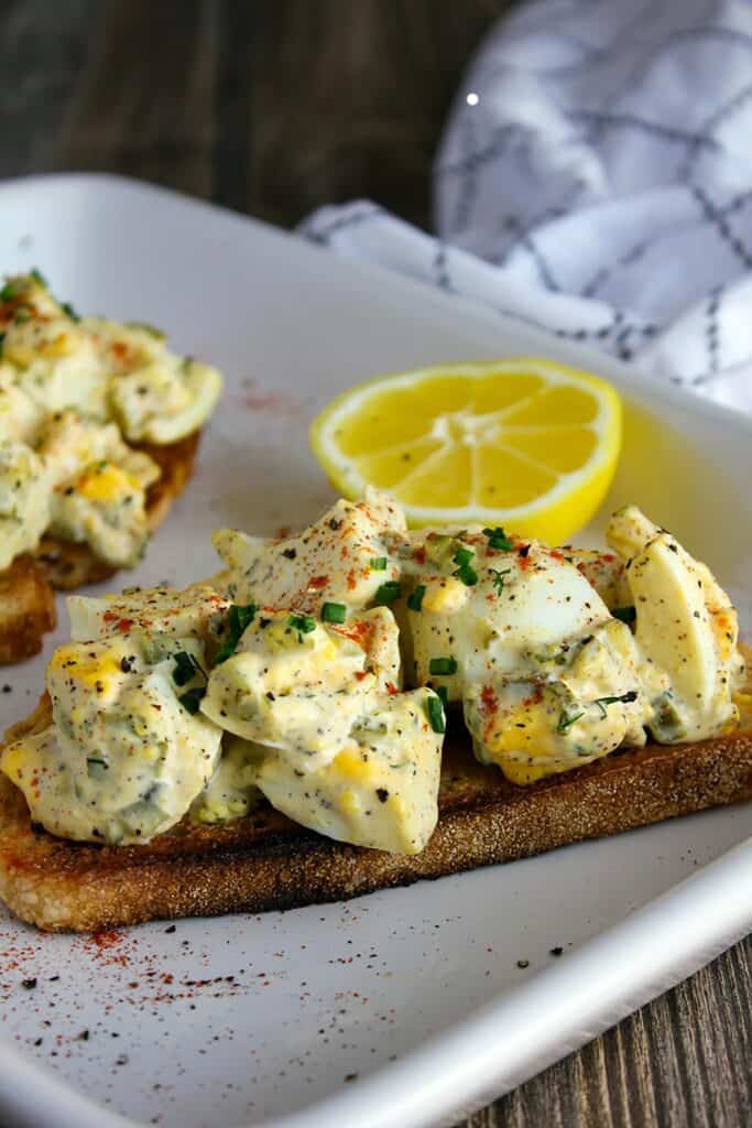 Two egg salad toasts with sliced lemon and towel.