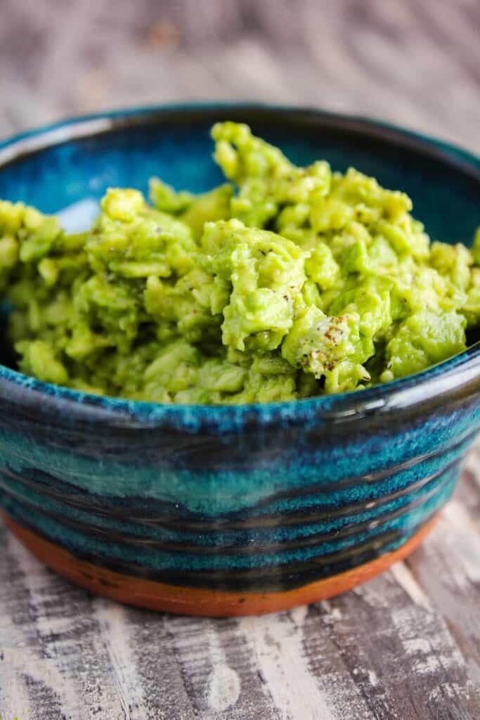 Mashed avocado in a blue bowl.