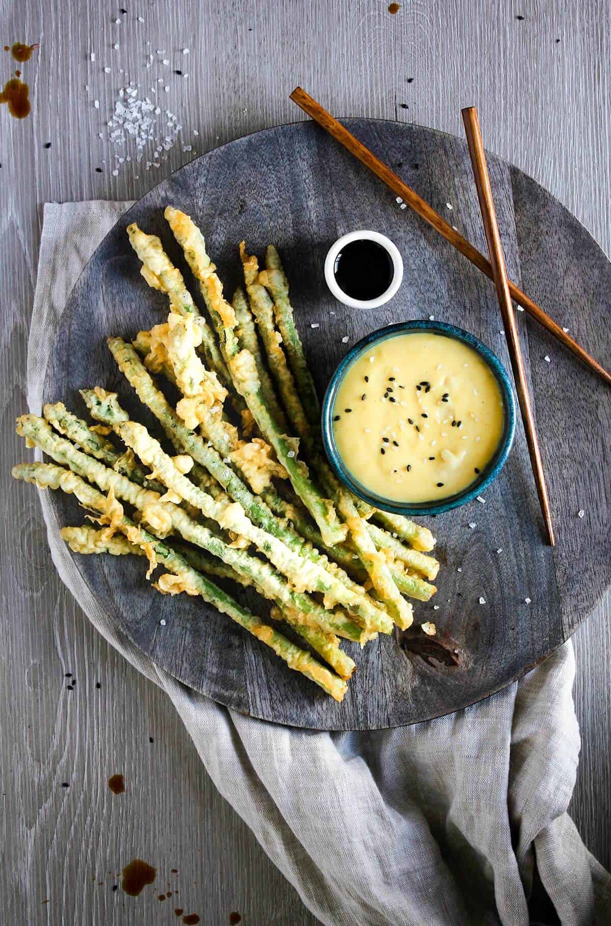 Asparagus tempura on a tray with bowl of miso aioli, soy sauce, and chop sticks.