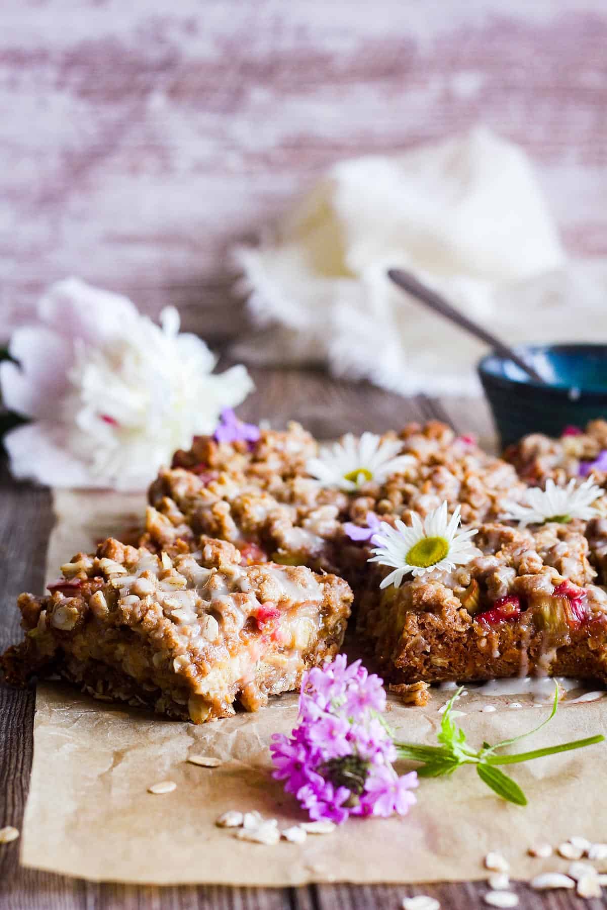 Rhubarb oatmeal bars with flowers and a bowl of glaze.