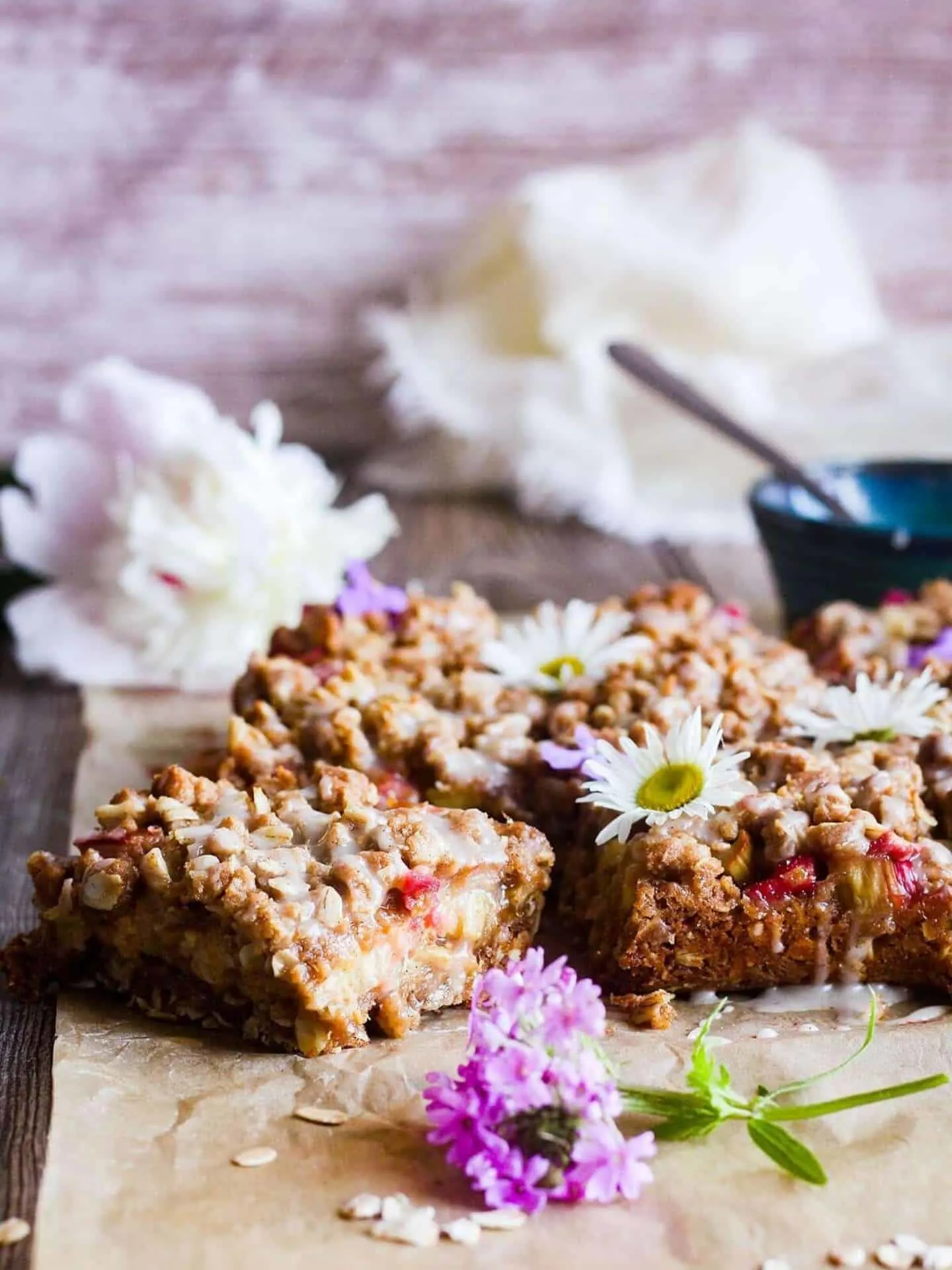 Rhubarb oatmeal bars with flowers and a bowl of glaze.