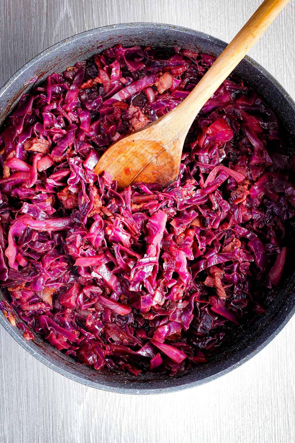 Braised cabbage with wooden spoon in pan.