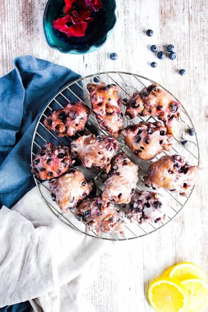 Wire cooling rack with berry fritters, scattered blueberries, and lemon slices.