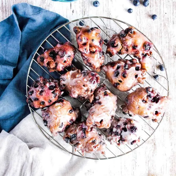 Wire cooling rack with berry fritters, scattered blueberries, and lemon slices.