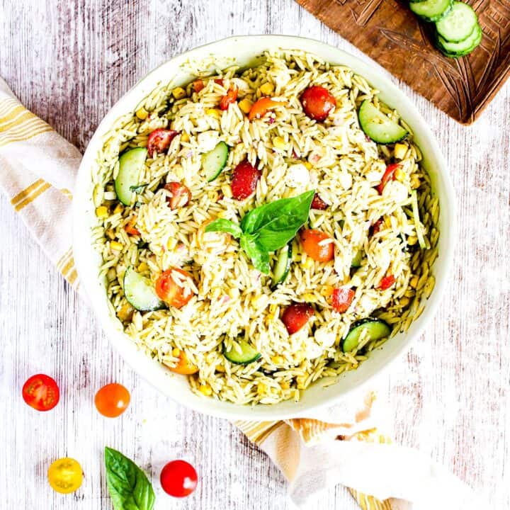 Serving bowl of pesto orzo salad with cherry tomatoes and sliced cucumber.