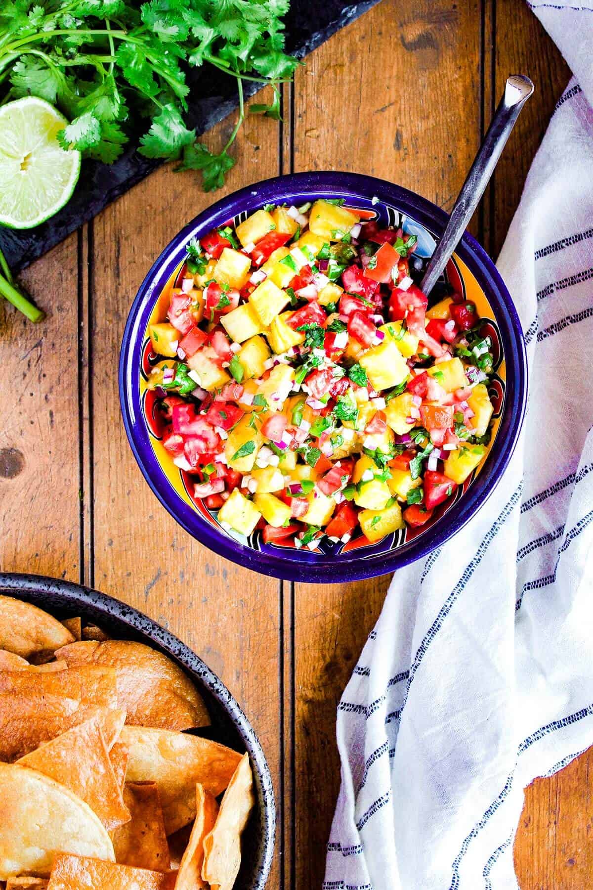 Bowl of pineapple pico and a bowl of chips with a lime and cilantro.
