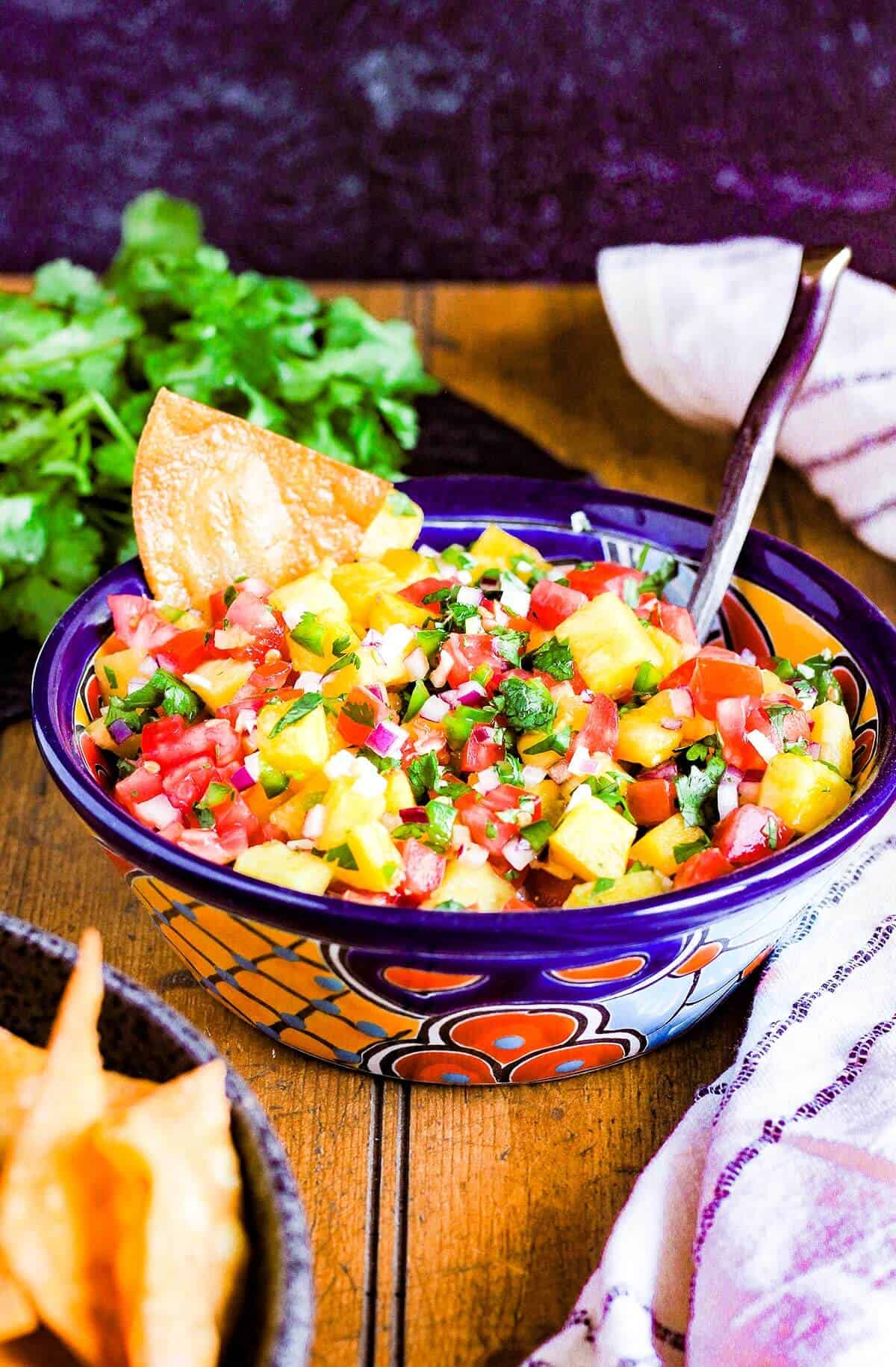 A bowl of pico, a bowl of chips, and a bunch of cilantro.