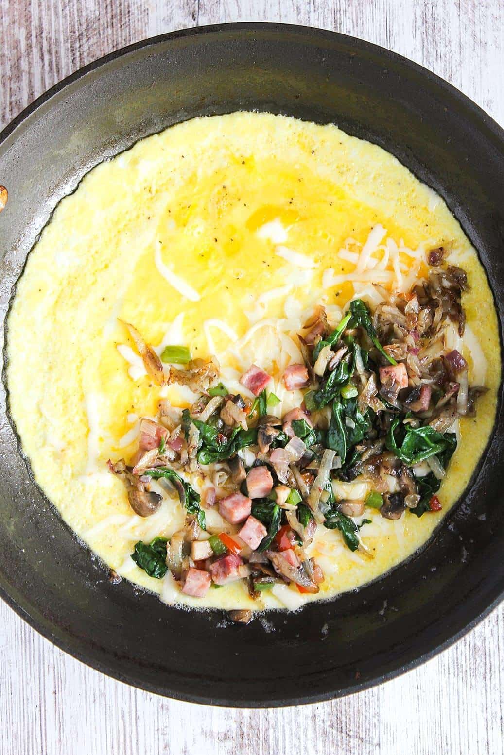 Eggs layered with cheese, veggies, and ham in a skillet.