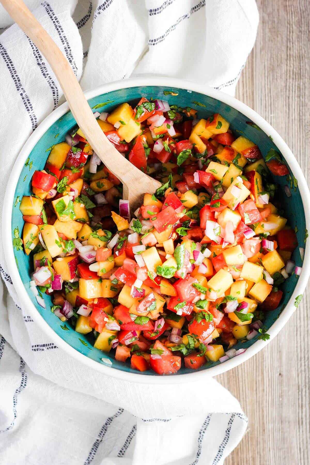 Mixed peach salsa in a bowl with a spoon.