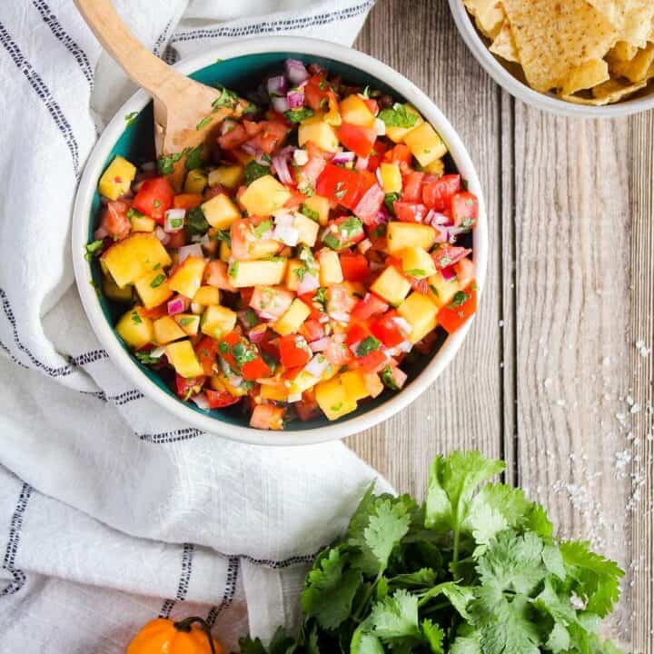 Bowl of fresh peach salsa with a bowl of chips and fresh produce.