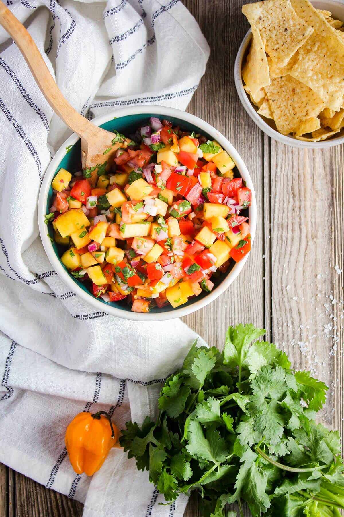 Bowl of fresh peach salsa with a bowl of chips and fresh produce.
