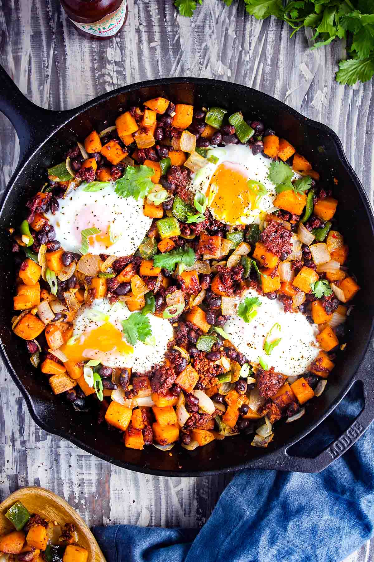Sweet potato hash with chorizo and eggs in a cast-iron skillet with a side of hot sauce.