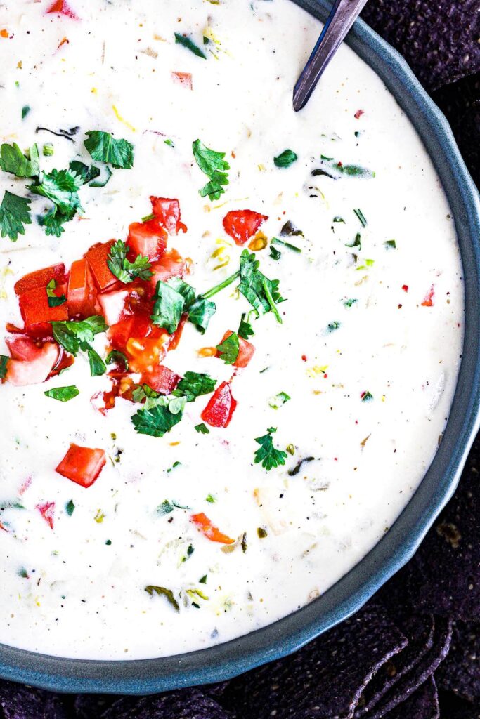 Close-up of homemade queso dip garnished with tomato and cilantro.